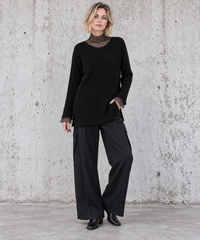 Black oversized rib-knit sweater on a blonde model in a relaxed pose with one hand in trouser pocket – Simple Moderne