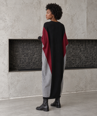 Rear three-quarter view of the oversized block knit midi dress, showing its black back, burgundy side panels and tapered grey hem.