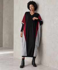 Model leaning against a concrete wall in the black oversized V-neck block knit midi dress, showing its loose drape and colour-block panels.