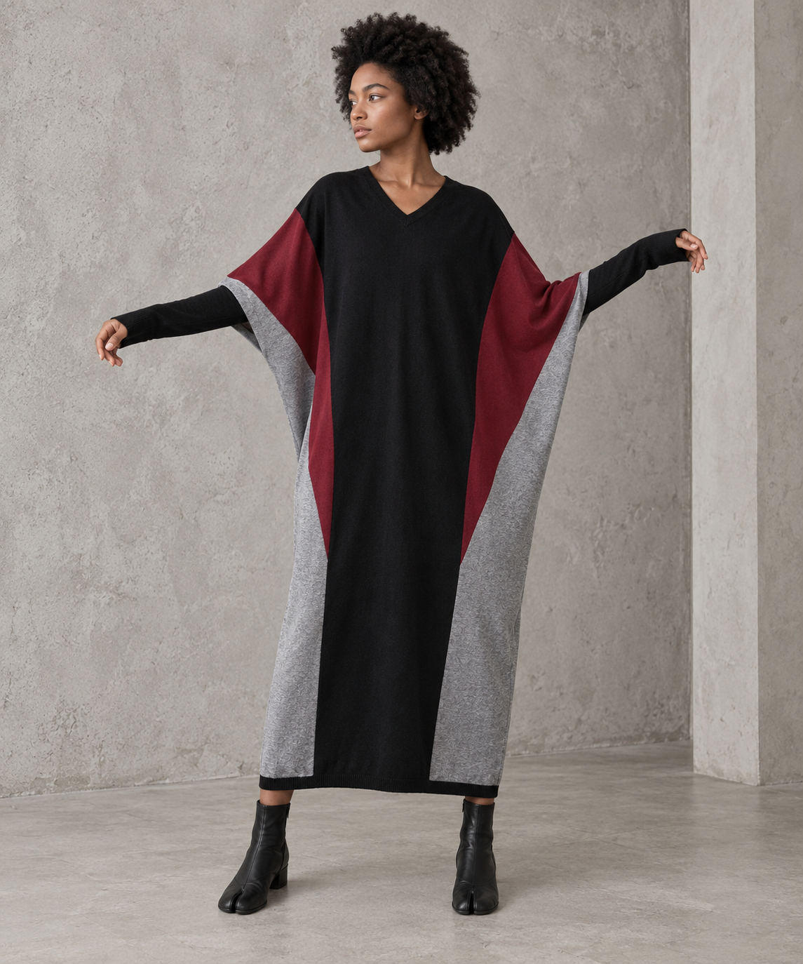 Black oversized V-neck block knit midi dress with arms raised softly to show the wide batwing sleeves and burgundy and grey panels.