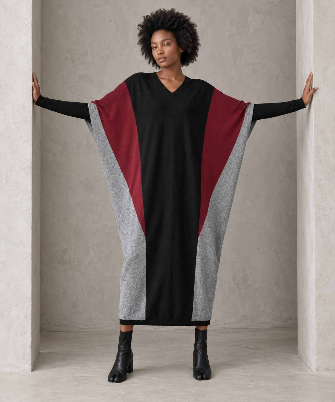 Full-length front view of the black oversized block knit midi dress with arms extended, showing its generous width and tapered hem.
