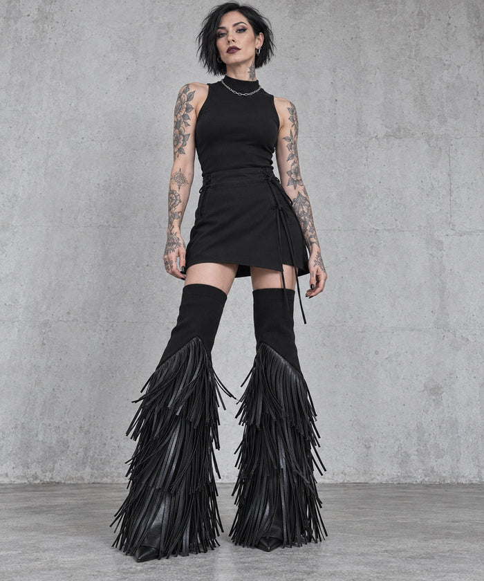 Black vegan leather tassel flare leg warmers on a tattooed gothic model, full-length front view styled with a short black skirt.