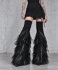 Close-up of black tassel flare leg warmers showing the separate upper cuffs and layered fringe over pointed black shoes.
