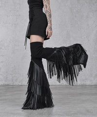 Side detail of black vegan leather tassel leg warmers with one knee bent, showing the hanging fringe and flared lower section.