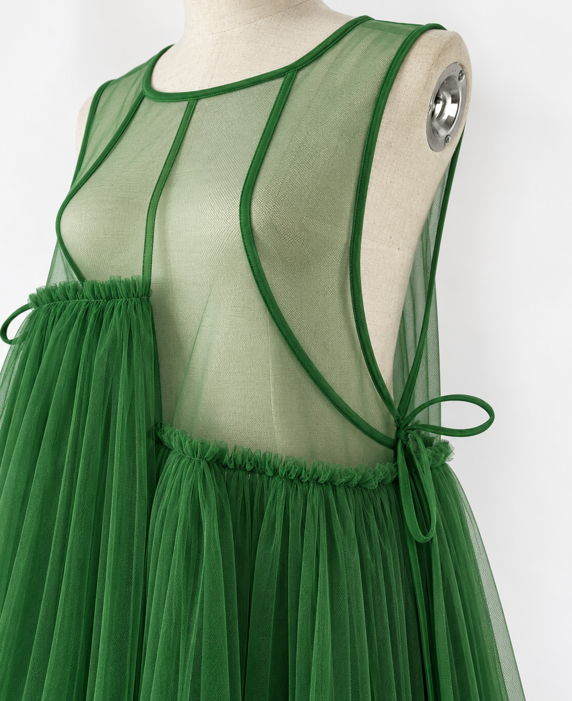 Green mesh dress on a cream mannequin, close-up of the sheer bodice, bound neckline, curved seams and side tie.