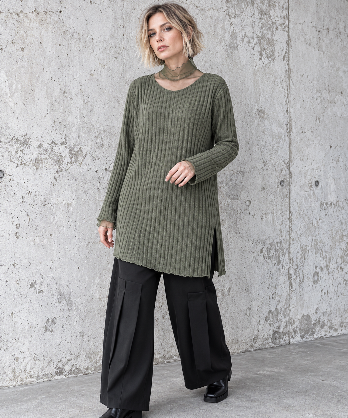Olive Green Oversized Turtleneck Knit Sweater. Three-quarter front view showing the olive sweater's vertical ribs, side split and sheer cuff extensions.