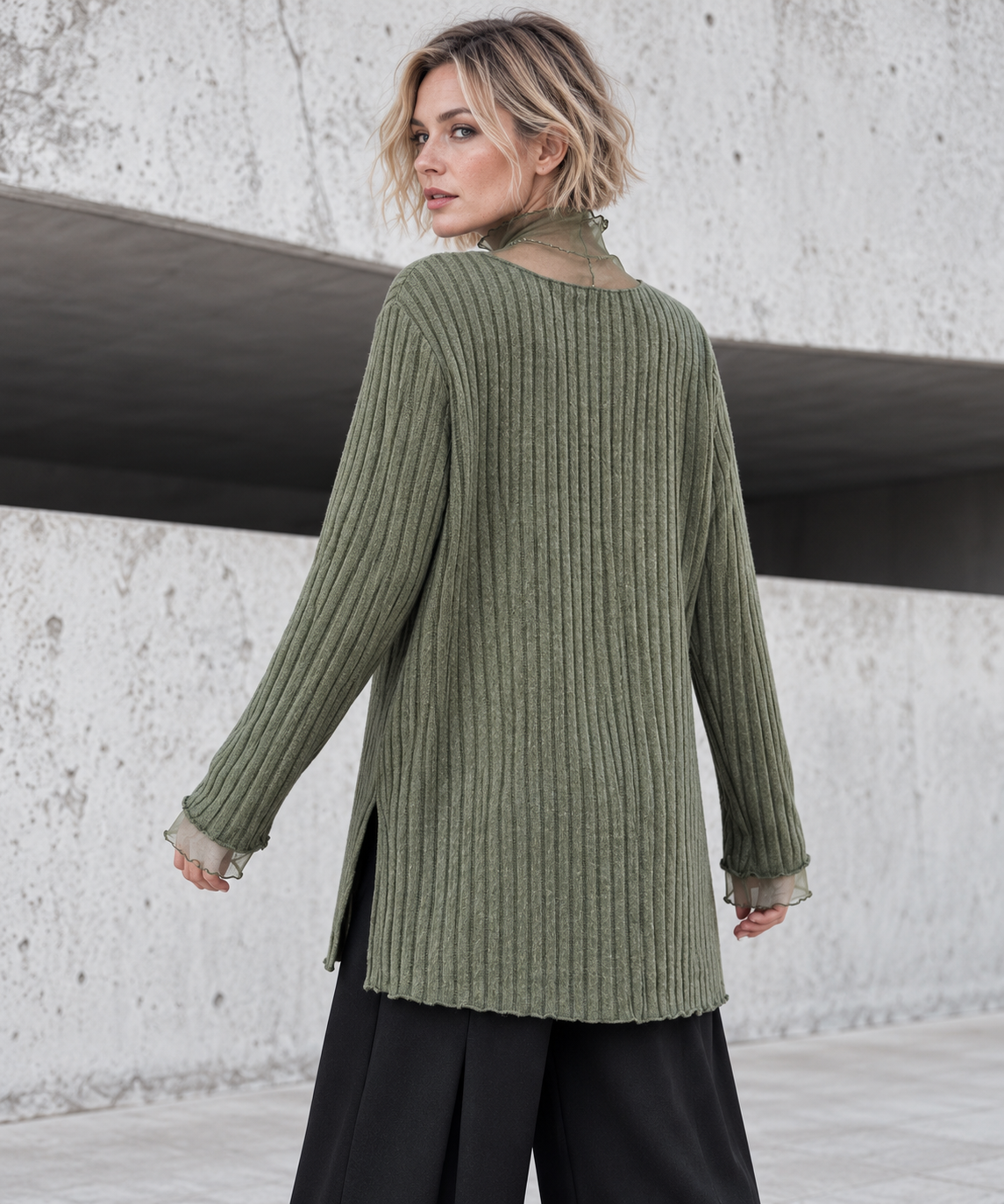Olive Green Oversized Turtleneck Knit Sweater. Back view on a blonde model, showing the olive vertical rib knit, relaxed shoulders and sheer high neck.