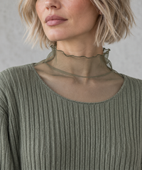 Olive Green Oversized Turtleneck Knit Sweater. Close-up of the sheer olive high neckline with a waved edge above the ribbed sweater's scoop neckline.