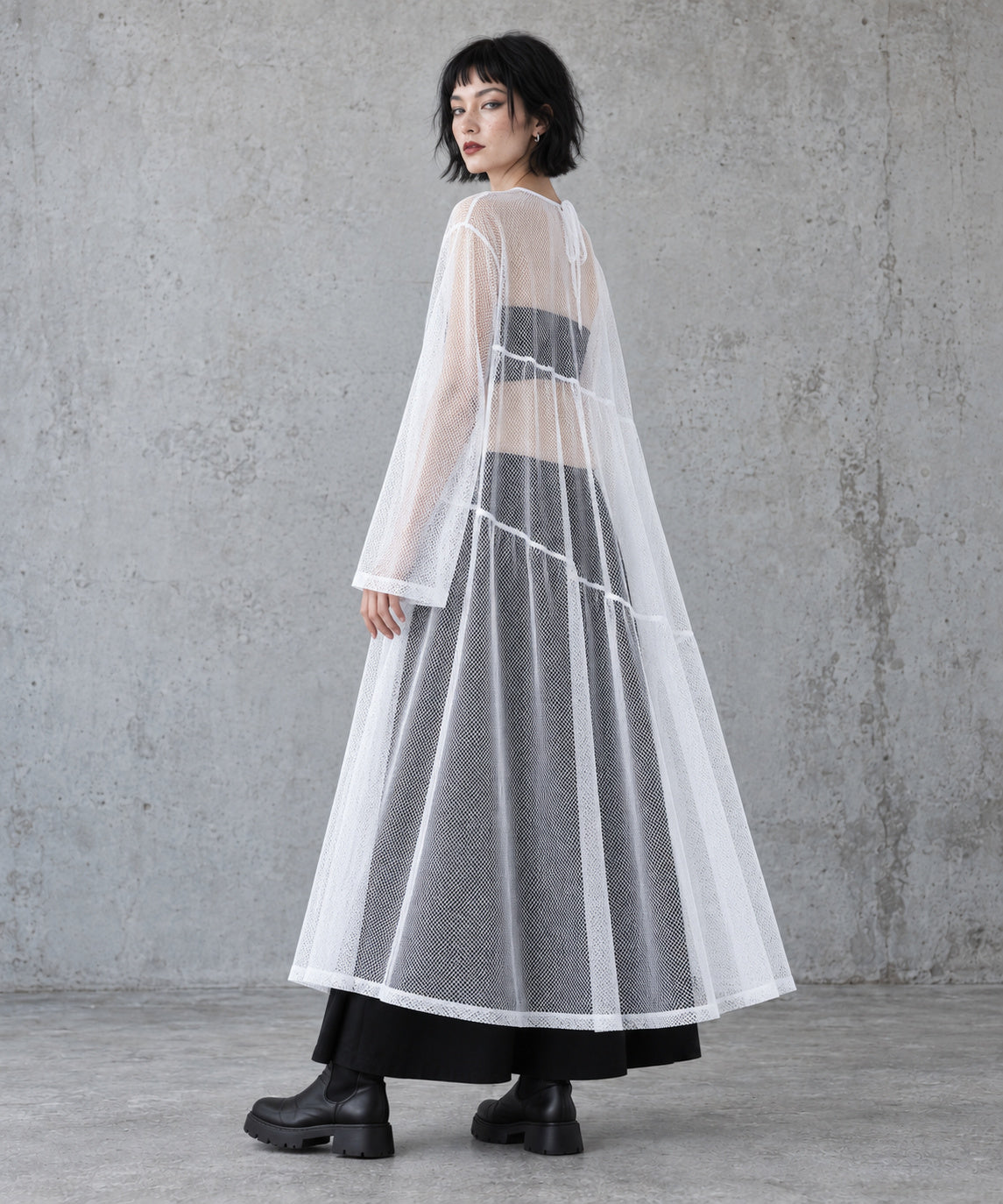 Rear three-quarter view of the white sheer A-line maxi dress showing the long sleeves and loose drape.