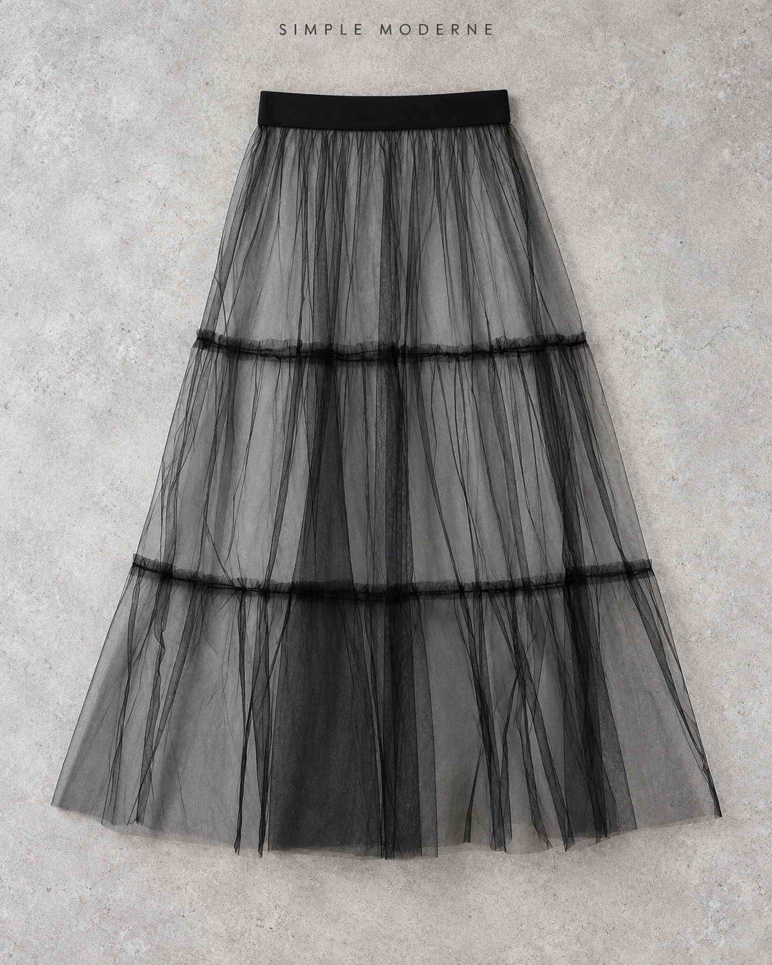 Black layered gauze overlay midi skirt displayed flat on a light concrete background.