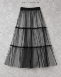 Black layered gauze overlay midi skirt displayed flat on a light concrete background.